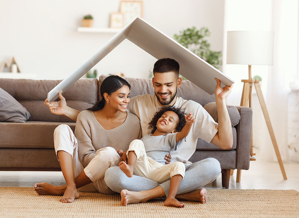 Family father, mother son in living room holding a paper roof over thier heads